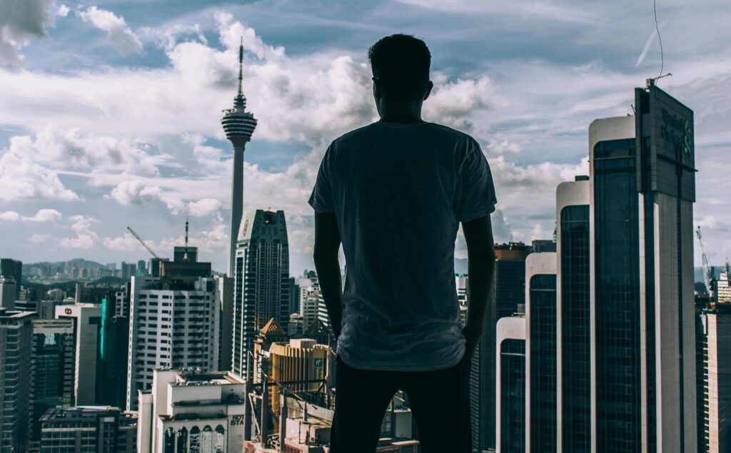 A silhouette of a man overlooking the Kuala Lumpur skyline, featuring the iconic KL Tower.